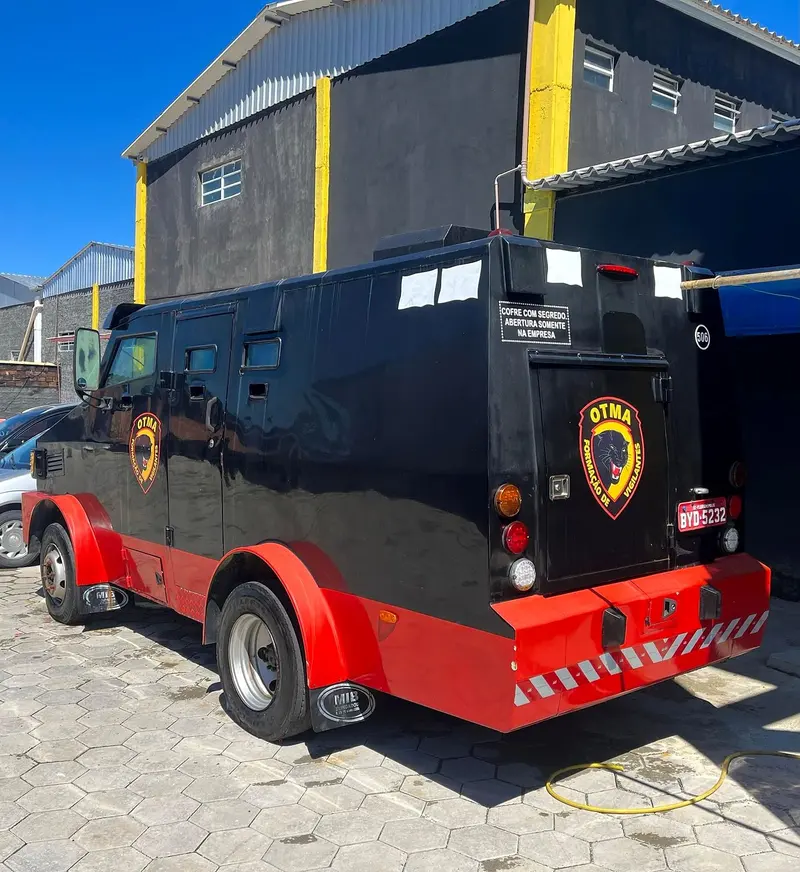 Carro-forte preto e vermelho com o escudo da OTMA, usado no treinamento de transporte de valores, no pátio da escola